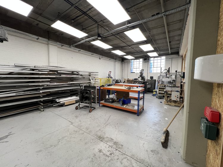 Metal stock racks and workshop equipment beneath an exposed industrial ceiling.