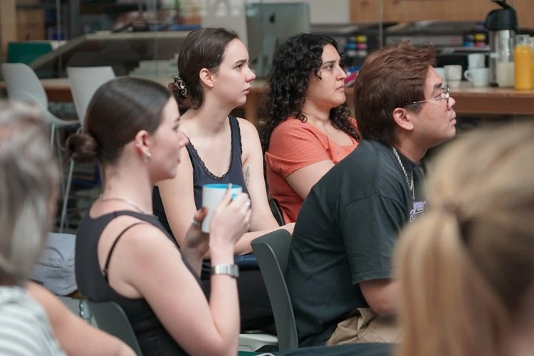 A group of people attentively listening during a meeting or presentation in an indoor setting.