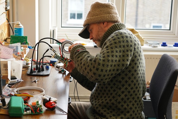 A maker soldering a small electronic device at a workbench