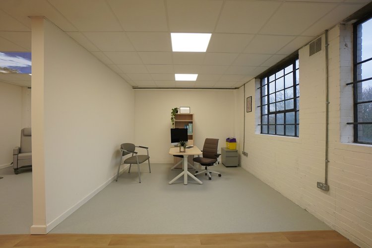 Consultation room with a desk, monitor, chairs and large windows.