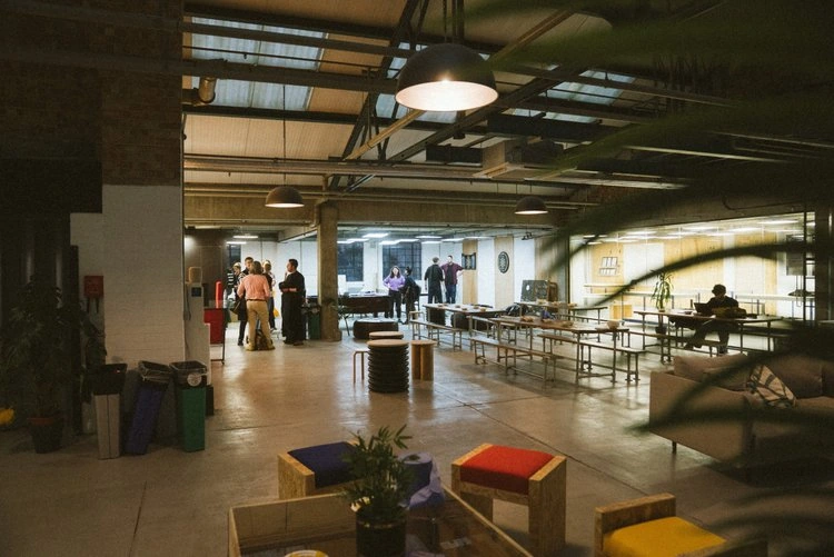 People gathering in an open shared space with tables and exposed roof beams.