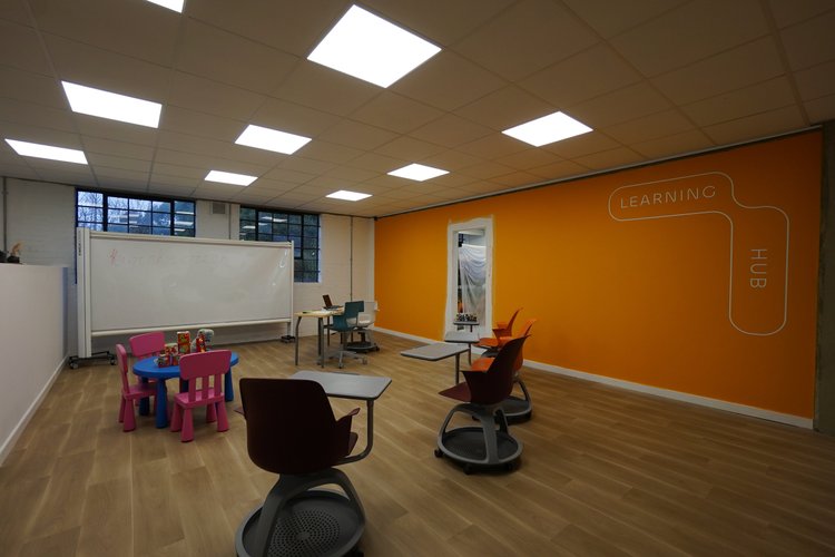 Learning room with tables, small chairs, a whiteboard and an orange wall.