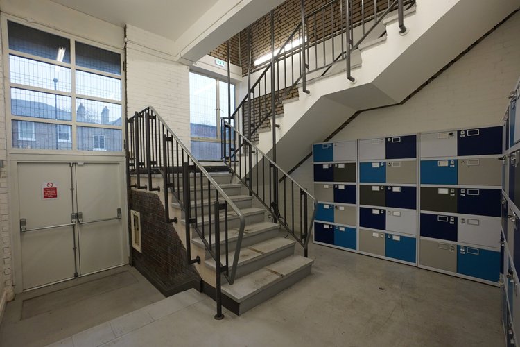 Industrial stairwell beside blue-and-white lockers and large windows.