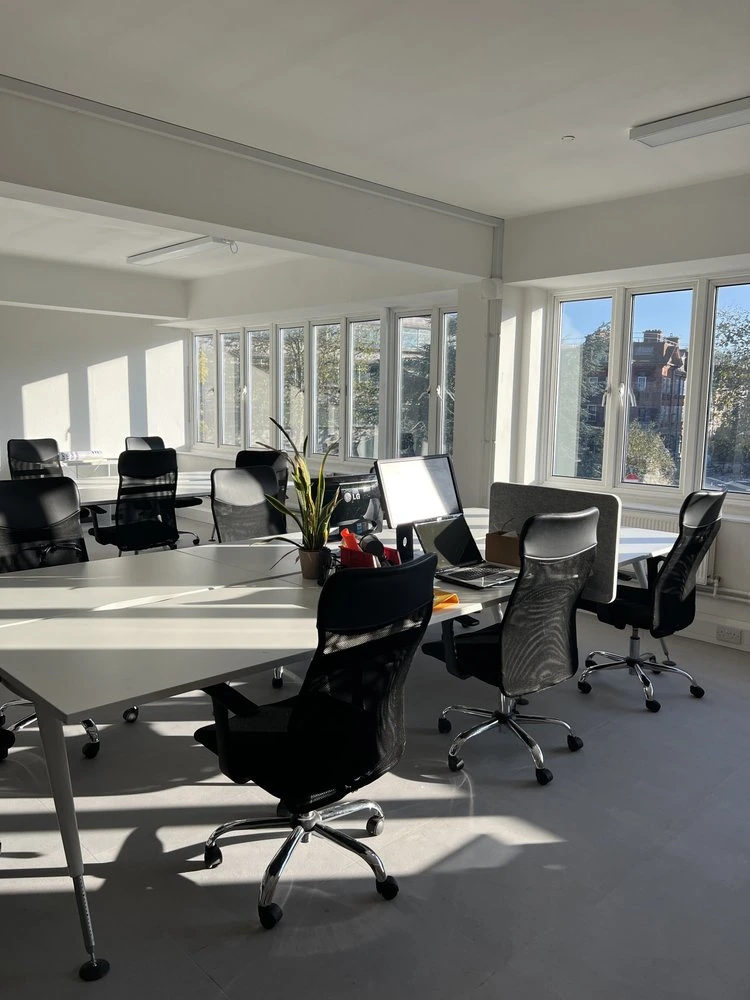 Sunlit shared office with white desks, office chairs and large windows.