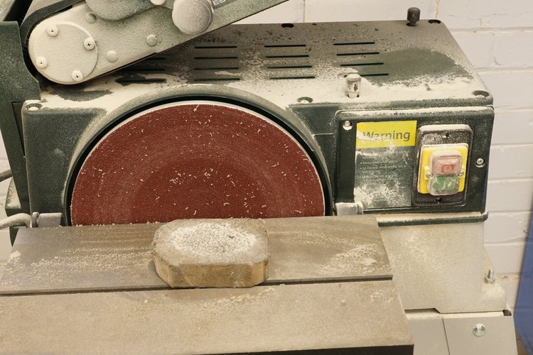A disc sander with a workpiece resting on its table.