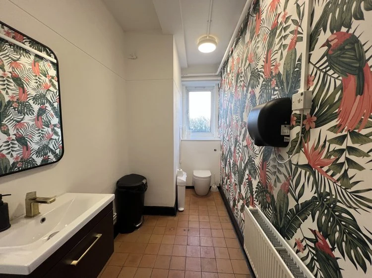Washroom with basins, flamingo-patterned wallpaper and a toilet beyond.