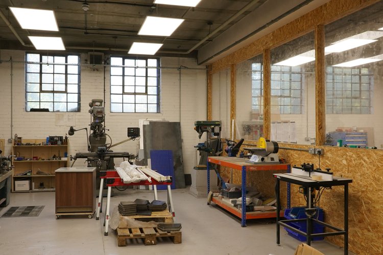 Workshop with machine tools, workbenches and large industrial windows.